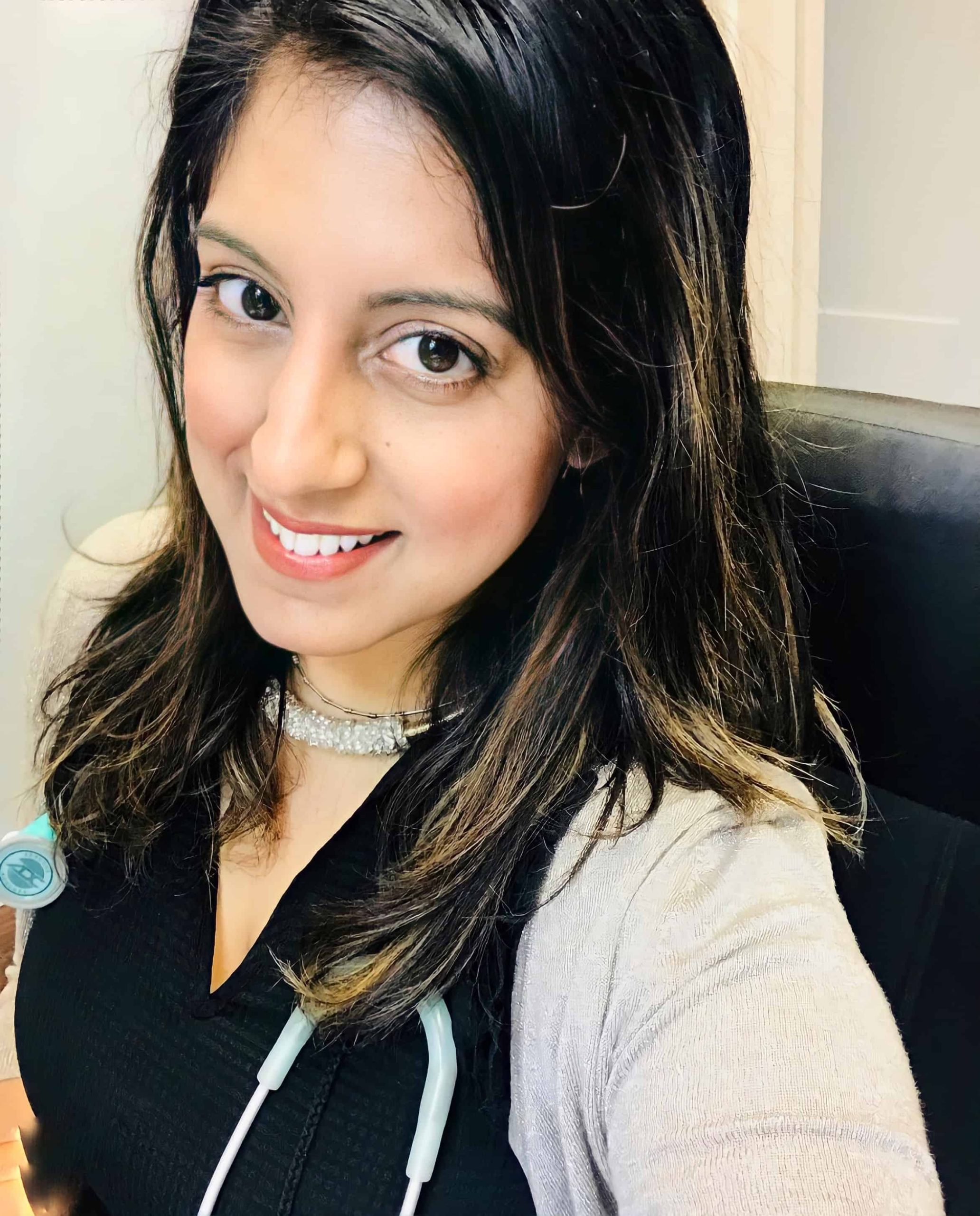 A woman with a stethoscope smiling at the camera in a professional setting.